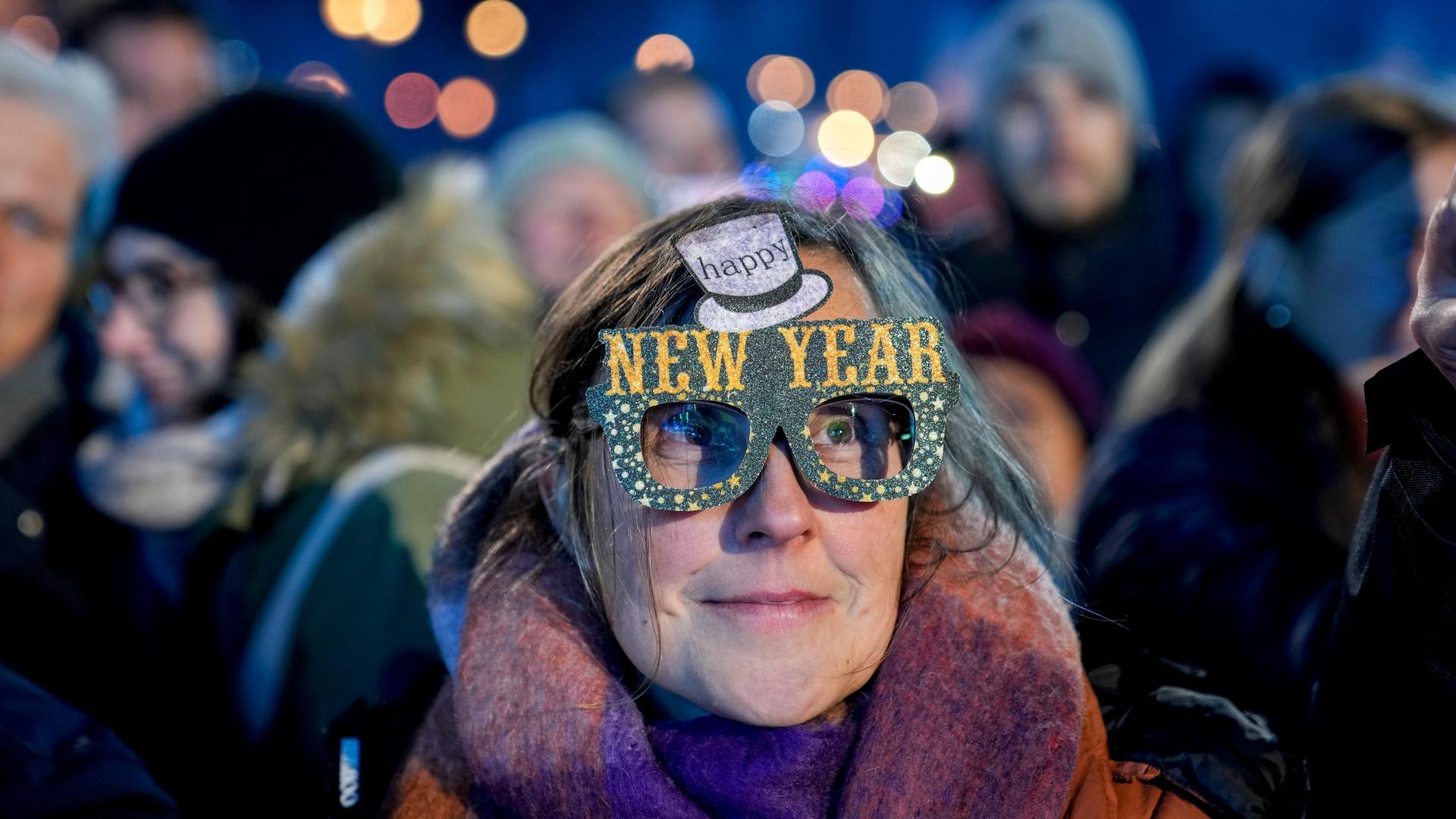 Eine Frau in einer Menschenmenge trägt eine bunte Pappbrille mit der Aufschrift "Happy New Year".