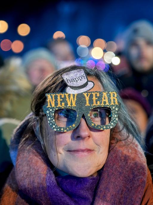 Eine Frau in einer Menschenmenge trägt eine bunte Pappbrille mit der Aufschrift "Happy New Year".