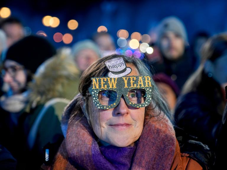 Eine Frau in einer Menschenmenge trägt eine bunte Pappbrille mit der Aufschrift "Happy New Year".