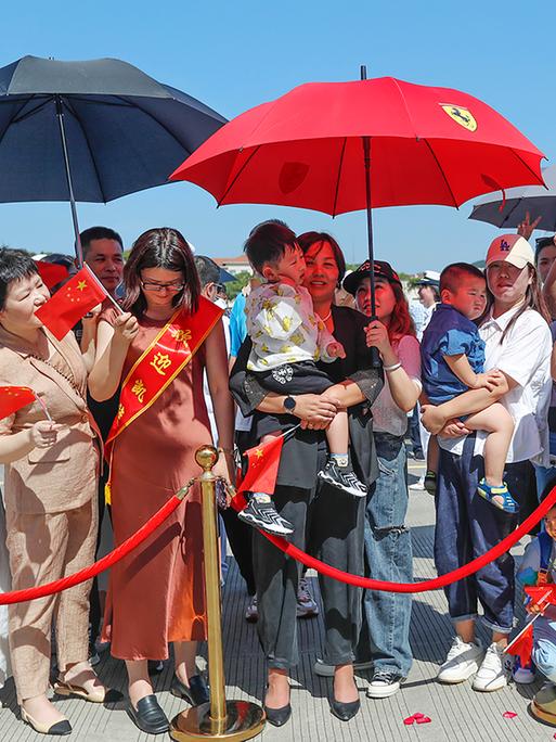 Familienangehörige von Soldaten in einem Hafen in China bei einer Begrüßungszeremonie. Das Schiff kehrt von einem Freundschaftsbesuch in Kiribati zurück.

