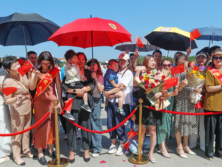 Familienangehörige von Soldaten in einem Hafen in China bei einer Begrüßungszeremonie. Das Schiff kehrt von einem Freundschaftsbesuch in Kiribati zurück.


