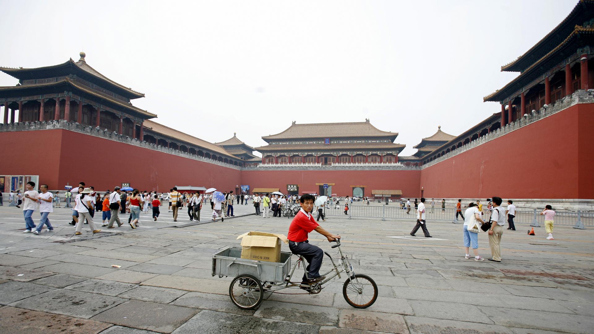 Ein Mann fährt mit einem Lastenfahrrad durch die Verbotene Stadt, während dort auch viele Touristen unterwegs sind.
