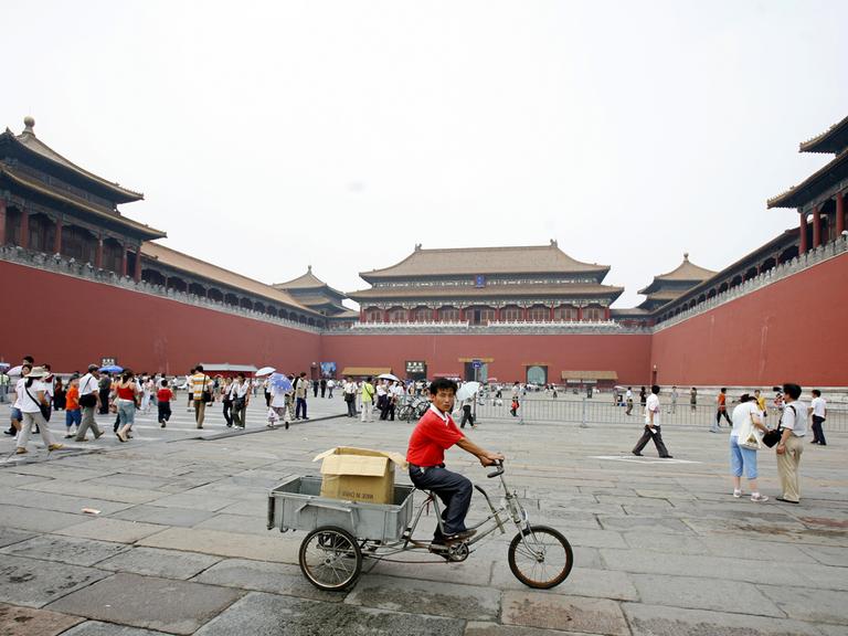 Ein Mann fährt mit einem Lastenfahrrad durch die Verbotene Stadt, während dort auch viele Touristen unterwegs sind.