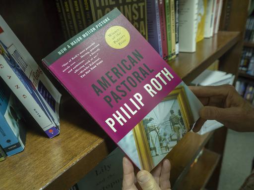 Ein Mann hält den Roman "Amerikanisches Idyll" (engl. "American Pastoral") von Philip Roth in den Händen.