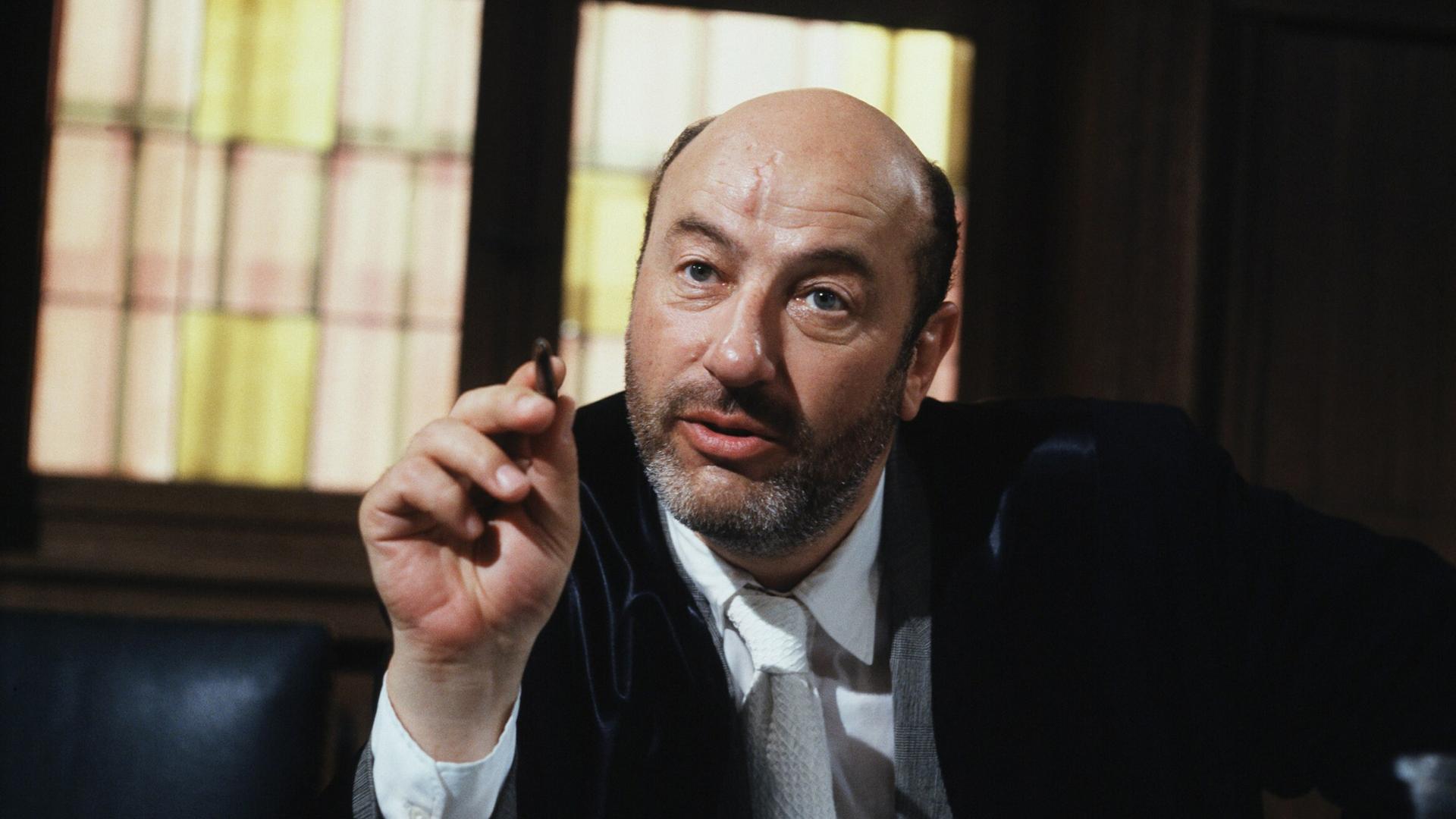 Manfred Krug in der Rolle des Anwalts Robert Liebling in der TV-Serie Liebling Kreuzberg. Er sitzt hinter einem massiven Schreibtisch und zeigt mit einem Stift in der rechten Hand nach vorn. Manfred Krug in der Rolle des Anwalts Robert Liebling in der TV-Serie Liebling Kreuzberg. Er sitzt hinter einem massiven Schreibtisch und zeigt mit einem Stift in der rechten Hand nach vorn.