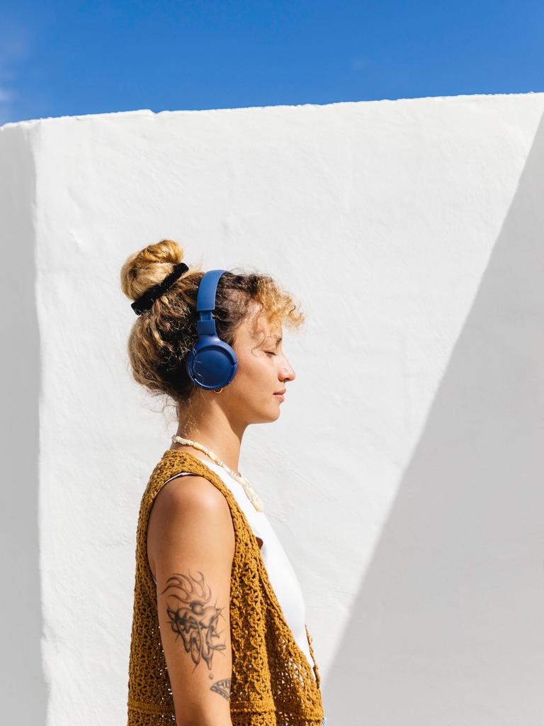 Eine Frau steht in der Sonne mit geschlossenen Augen und trägt einen Kopfhörer. 