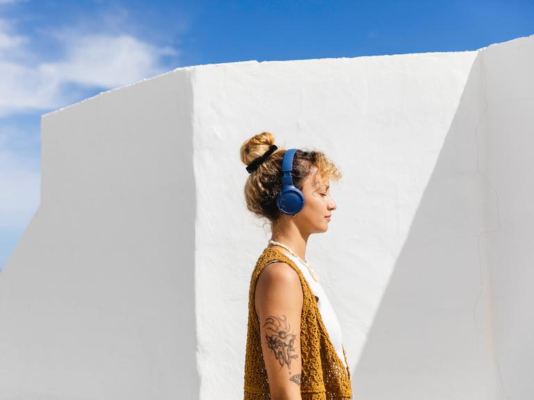 Eine Frau steht in der Sonne mit geschlossenen Augen und trägt einen Kopfhörer. 