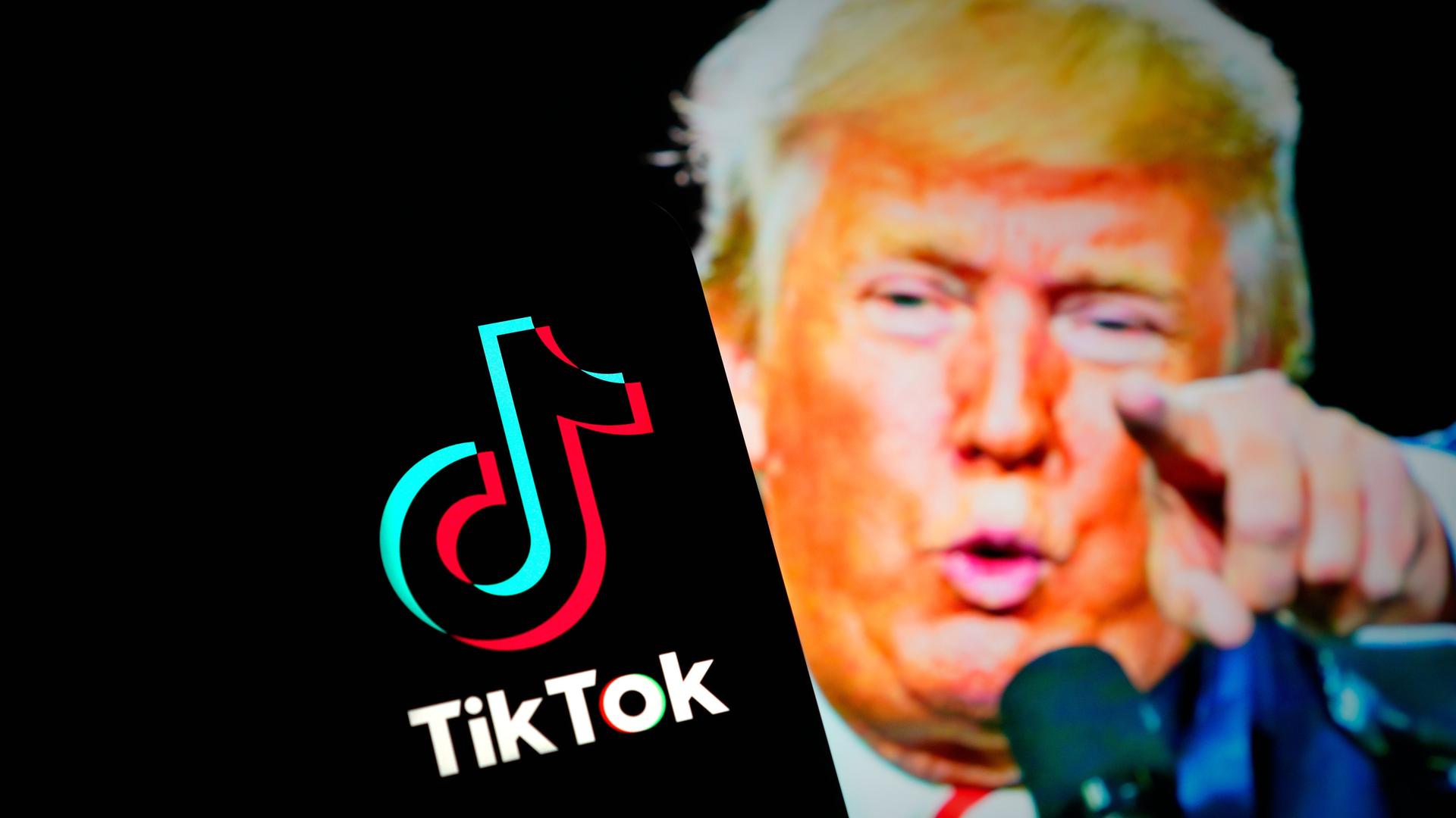 Ein Handybildschirm zeigt das Logo von Tiktok, im Hintergrund ist das Gesicht von Donald Trump zu sehen.