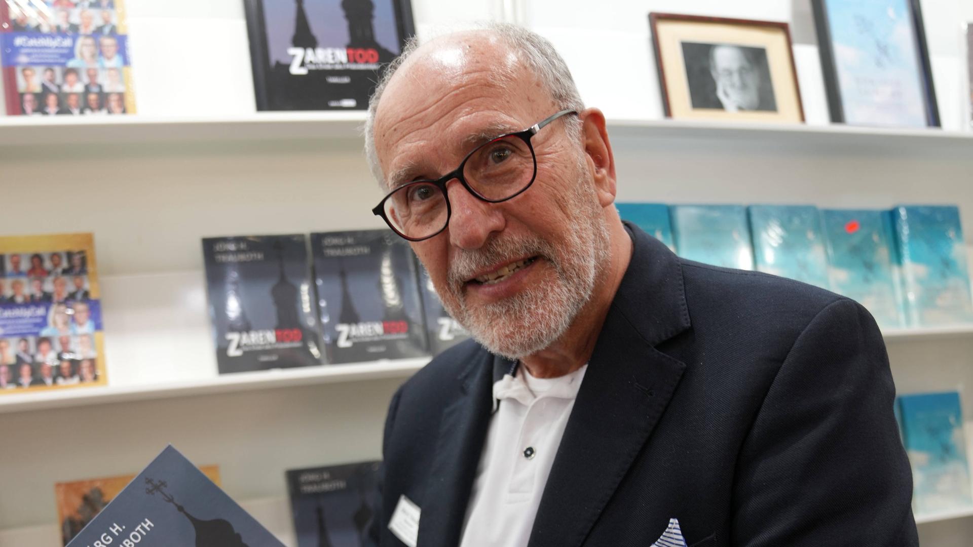 Jörg H. Trauboth lacht in die Kamera. Er steht in einer Buchhandlung und hält sein eigenes Buch "Zarentod" in der Hand. Jörg H. Trauboth lacht in die Kamera. Er steht in einer Buchhandlung und hält sein eigenes Buch "Zarentod" in der Hand.