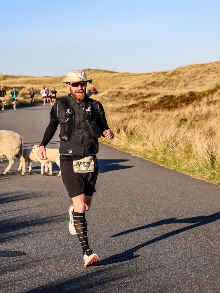 Teilnehmer am North Sea Ultra Marathon 2026 auf Sylt laufen durch die nordfriesische Landschaft auf der Insel. Zwischen zwei Läufern kreuzen Schafe den Weg in der Dünenlandschaft. Teilnehmer am North Sea Ultra Marathon 2026 auf Sylt laufen durch die nordfriesische Landschaft auf der Insel. Zwischen zwei Läufern kreuzen Schafe den Weg in der Dünenlandschaft.