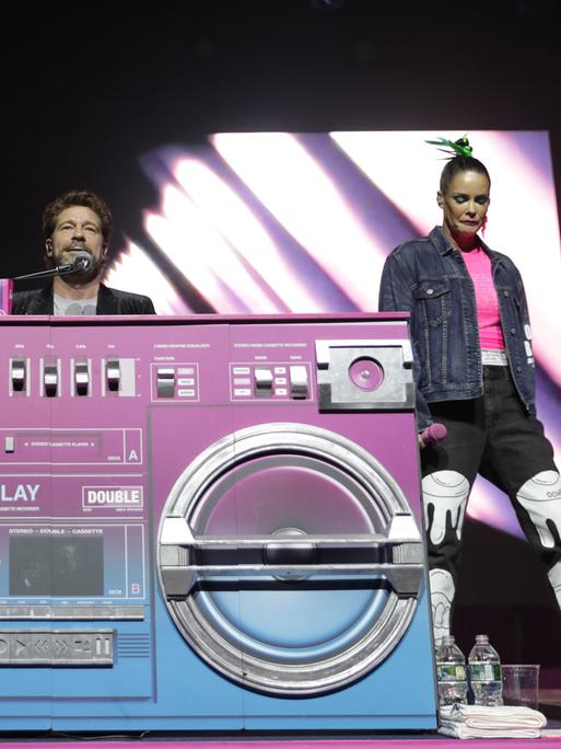 AQUA-Musiker Lene Nystrom, Rene Dif und Soren Rasted vor einem überdimensionierten pinken Radio auf einer Bühne