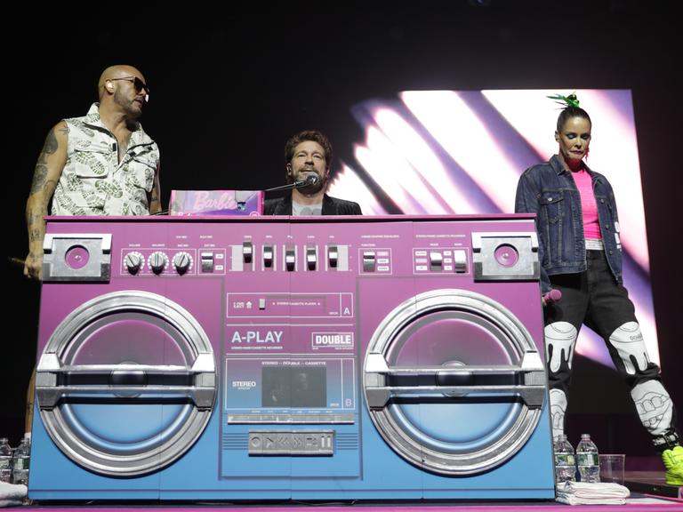 AQUA-Musiker Lene Nystrom, Rene Dif und Soren Rasted vor einem überdimensionierten pinken Radio auf einer Bühne