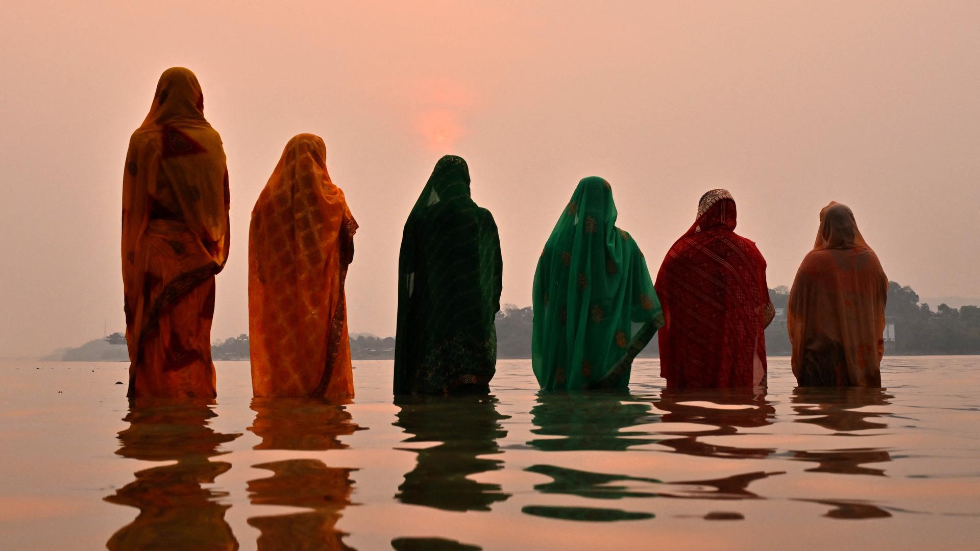 Bund gegkleidete Frauen in Indien stehen bei Sonnenuntergang hüfttief im Wasser. 