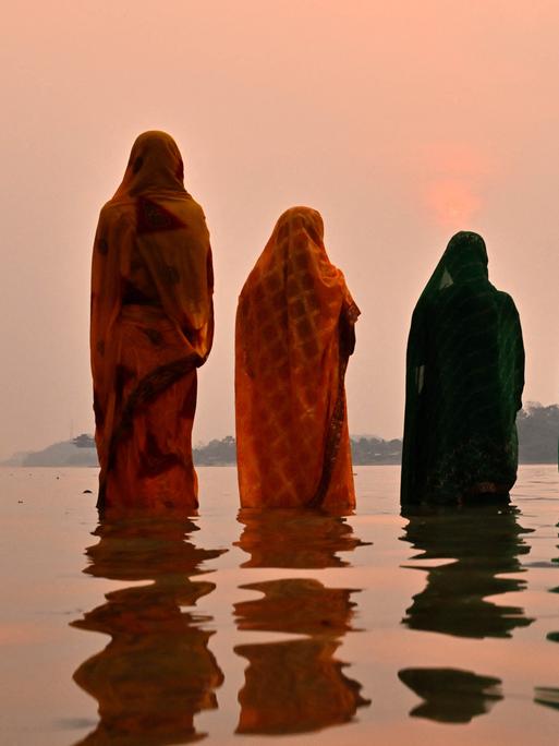 Bund gegkleidete Frauen in Indien stehen bei Sonnenuntergang hüfttief im Wasser. 