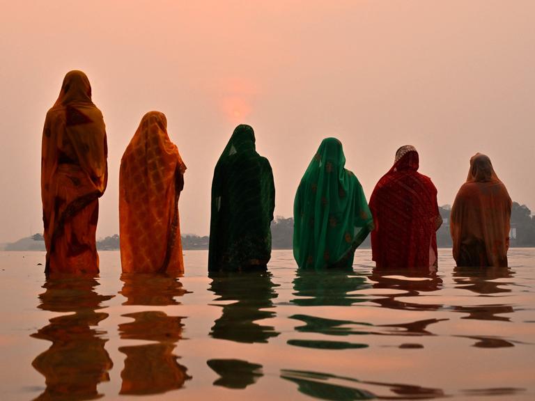 Bund gegkleidete Frauen in Indien stehen bei Sonnenuntergang hüfttief im Wasser. 