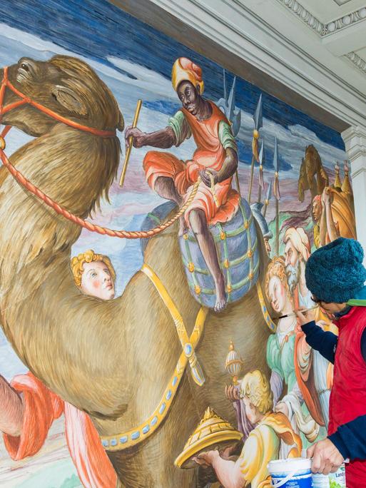 Rekonstruktionsarbeiten an einem Bild im Dresdener Residenzschloss. Eine Frau malt an einem Wandbild, das ein Kamel mit Reiter zeigt.