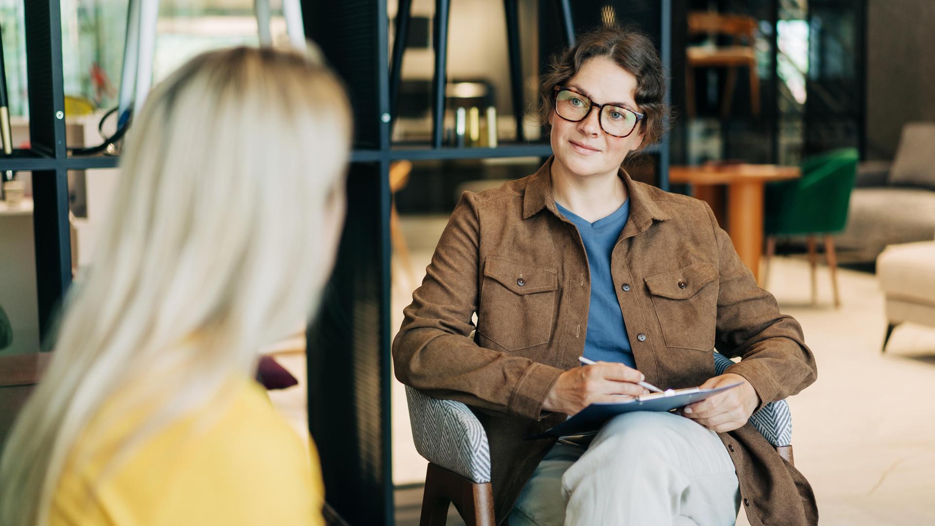 Eine Psycho-Therapeutin hört einer Patientin zu und macht sich Notizen. 