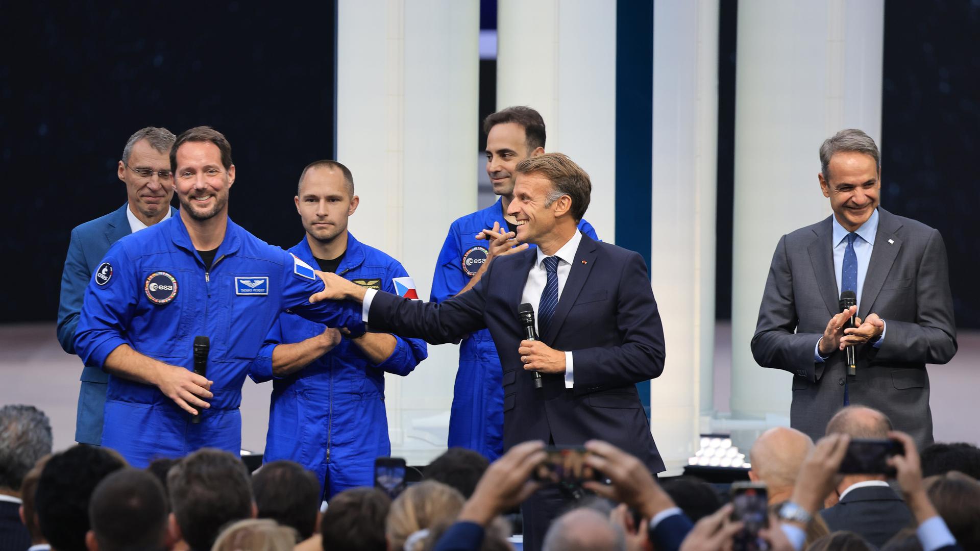 Der französische Präsident Macron steht zwischen dem Astronauten Thomas Pesquet und dem griechischen Premierminister Kyriakos Mitsotakis und hält ein Mikrofon in der Hand. Der französische Präsident Macron steht zwischen dem Astronauten Thomas Pesquet und dem griechischen Premierminister Kyriakos Mitsotakis und hält ein Mikrofon in der Hand.