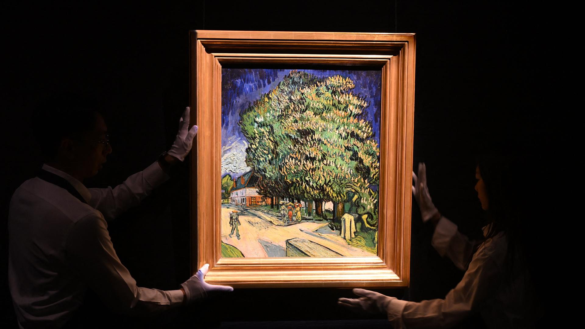 Im Dunkeln halten zwei Mitarbeitenden das Gemälde "Blühende Kastanienbäume" von Vincent Van Gogh, das hell erleuchtet ist