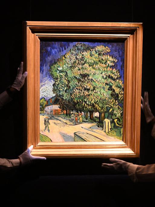 Im Dunkeln halten zwei Mitarbeitenden das Gemälde "Blühende Kastanienbäume" von Vincent Van Gogh, das hell erleuchtet ist
