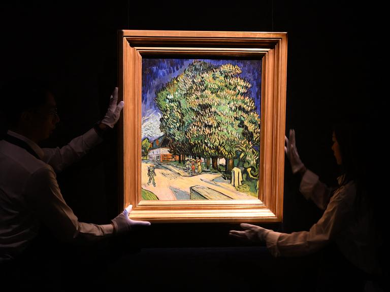 Im Dunkeln halten zwei Mitarbeitenden das Gemälde "Blühende Kastanienbäume" von Vincent Van Gogh, das hell erleuchtet ist