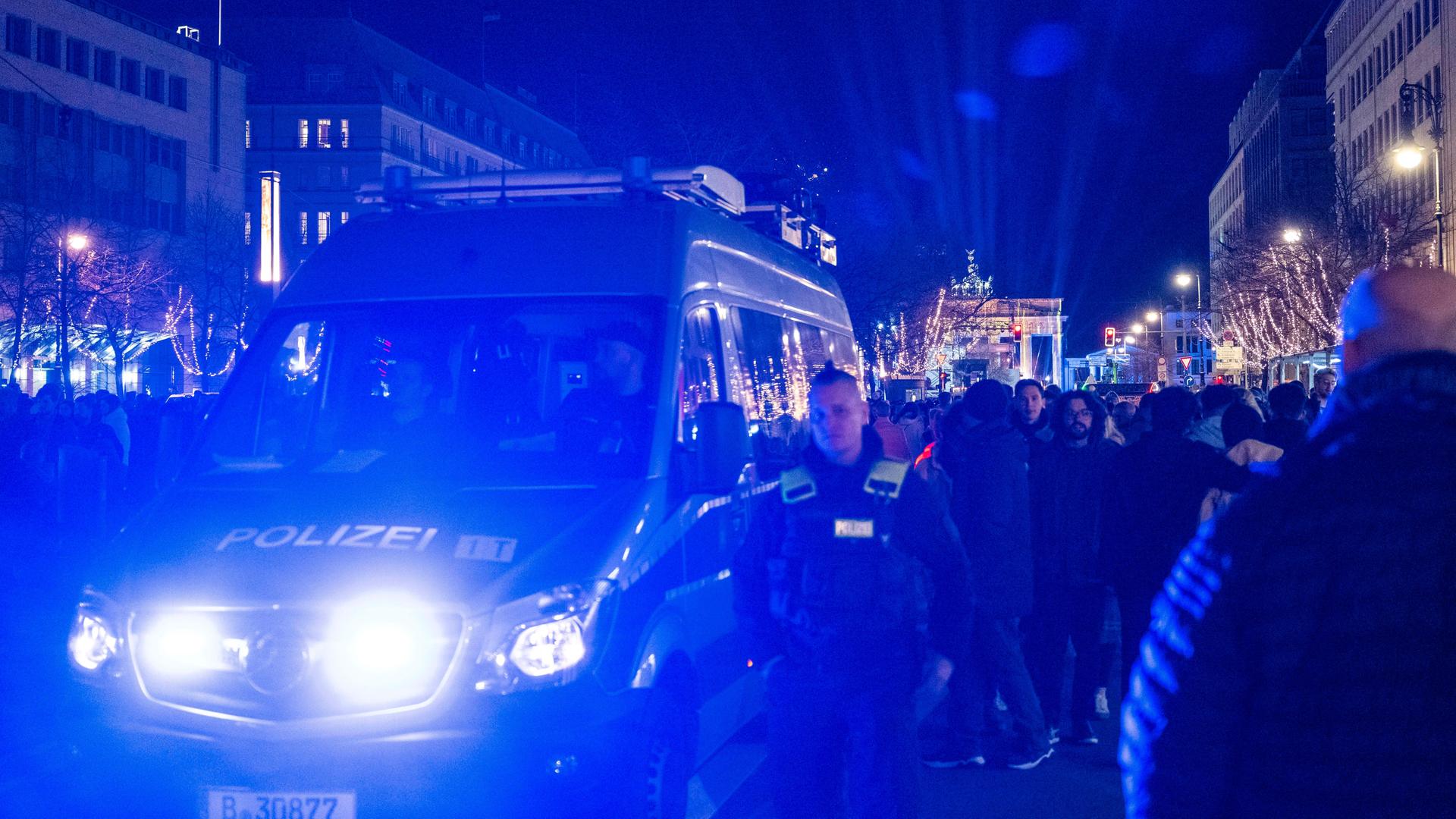 Ein Polizeiauto fährt vor dem Brandenburger Tor mit Blaulicht durch die Menschenmenge.