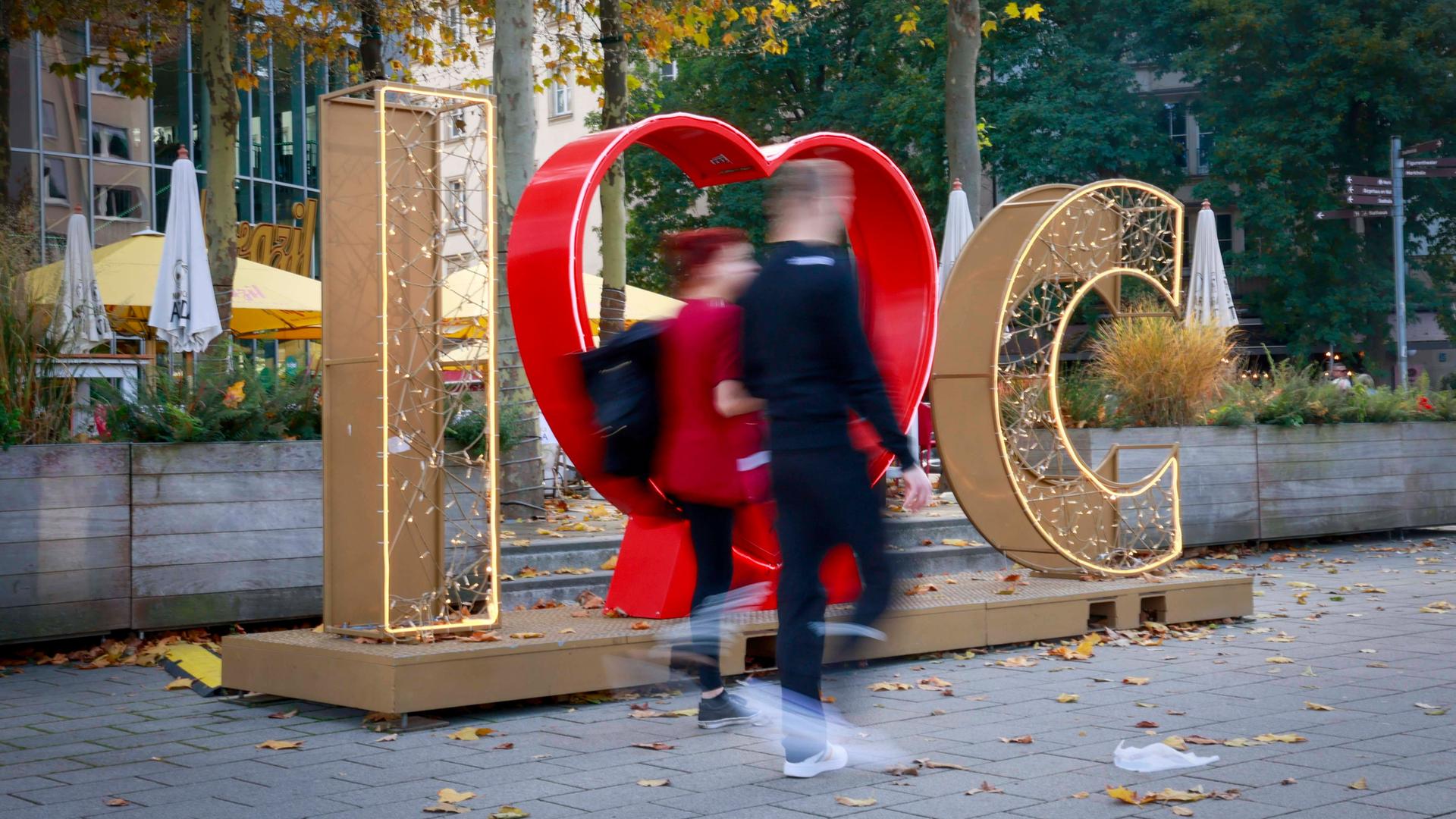 Zwei Menschen laufen durch die Innenstadtz von Chemnitz, hinter ihnen sieht man den erleuchteten Schriftzug "I love Chemnitz"