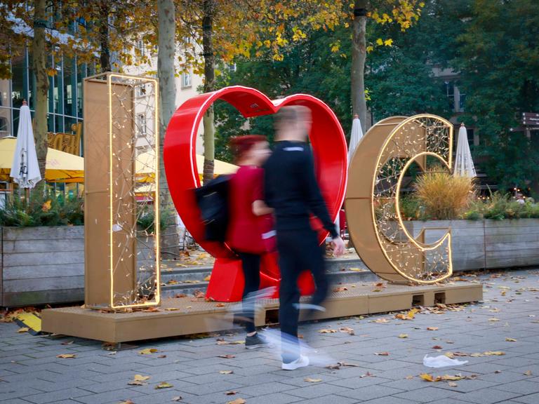 Zwei Menschen laufen durch die Innenstadtz von Chemnitz, hinter ihnen sieht man den erleuchteten Schriftzug "I love Chemnitz"