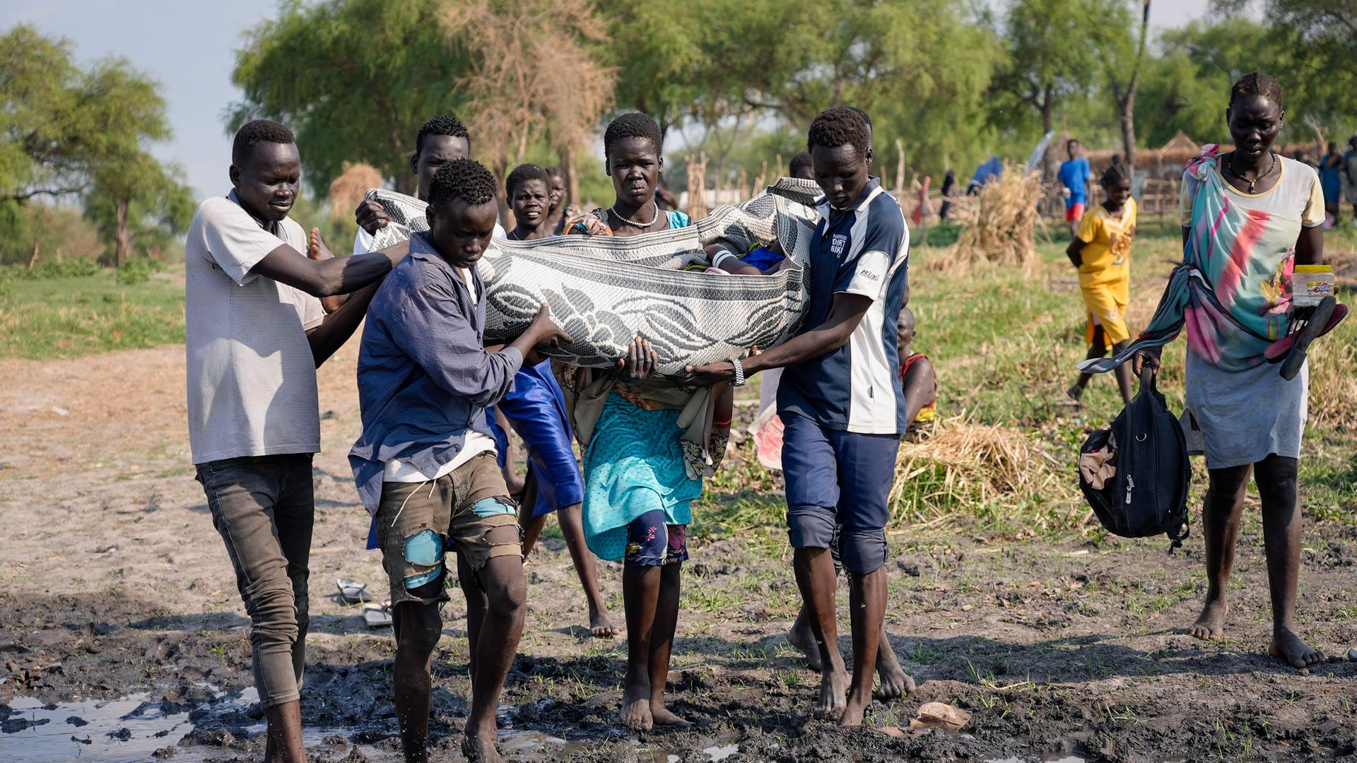 Sudan, Canal-Pigi: Dorfbewohner tragen eine kranke Frau zu einem Boot des Internationalen Medizinischen Korps, das sie in eine nahegelegene Stadt bringen soll. Die Region verfügt nur über begrenzten Zugang zu medizinischer Versorgung und wenige Straßen.
