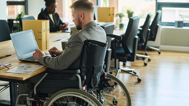 Ein Mann mit Rollstuhl arbeitet in einem Büro.