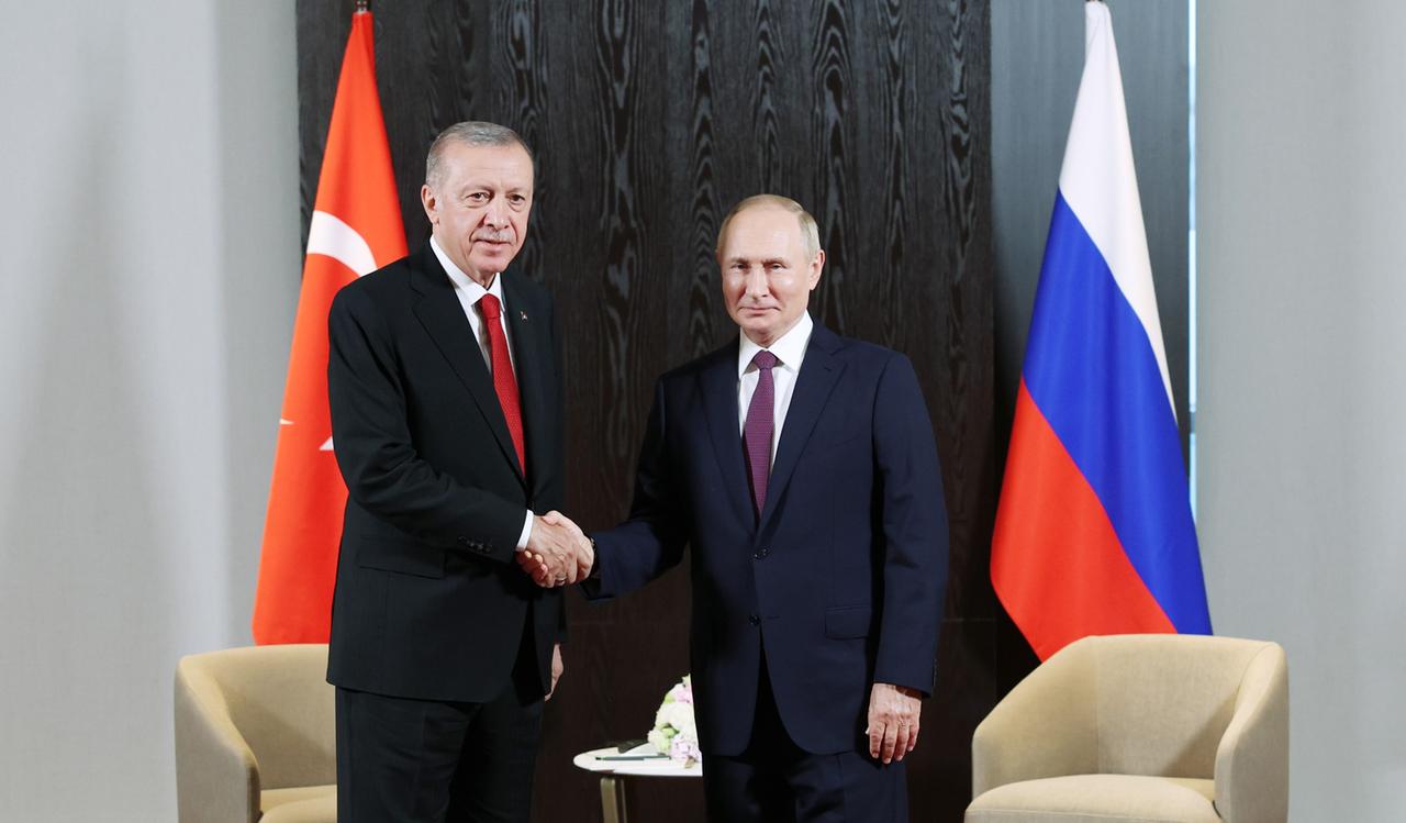 Recep Tayyip Erdogan und Wladimir Putin schütteln einander vor einer türkischen und einer russischen Flagge die Hände.