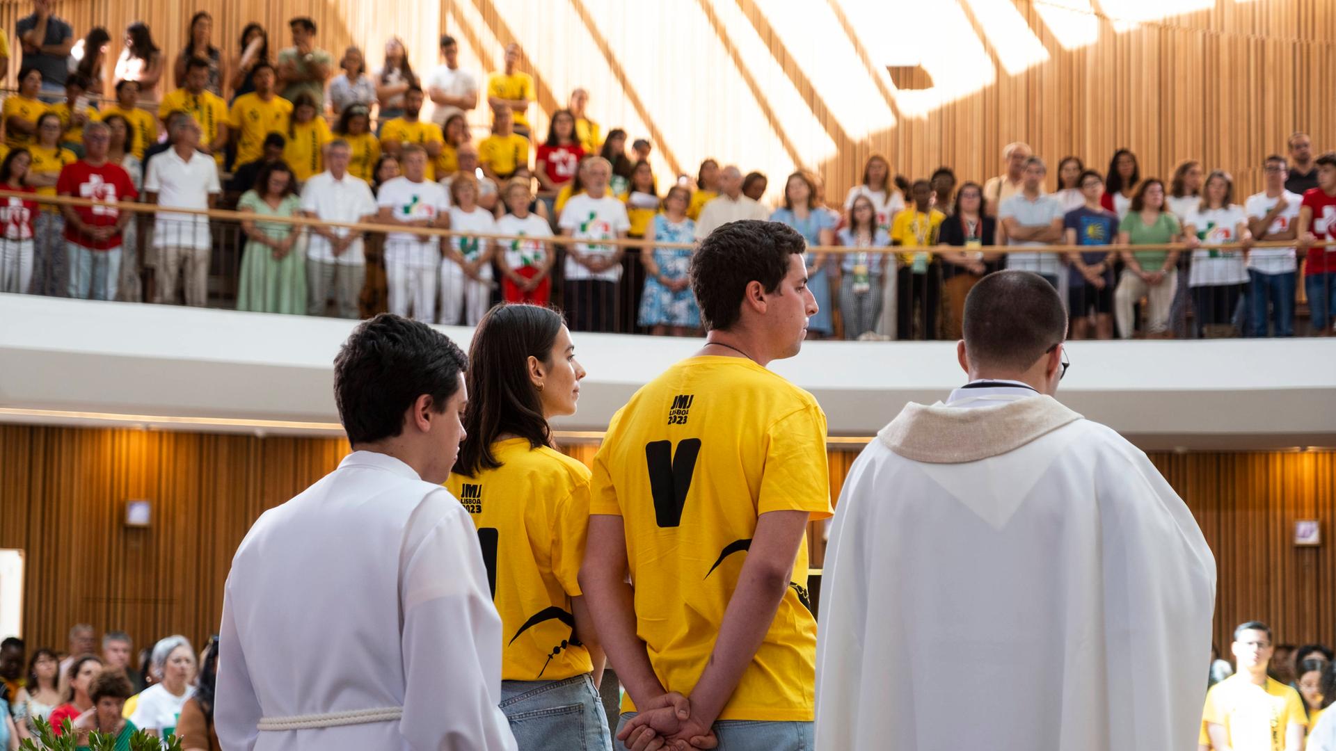 Junge Menschen in Sweatshirts des Weltjugendtages in Portugal stehen in einer Kirche in Lissabon.