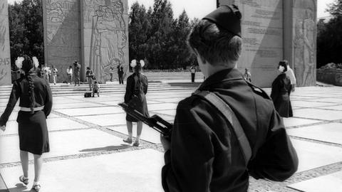 Jugendliche in der UdSSR stehen mit dem Rücken vor einem Denkmal in Uniform, die Jungen mit Gewehren.