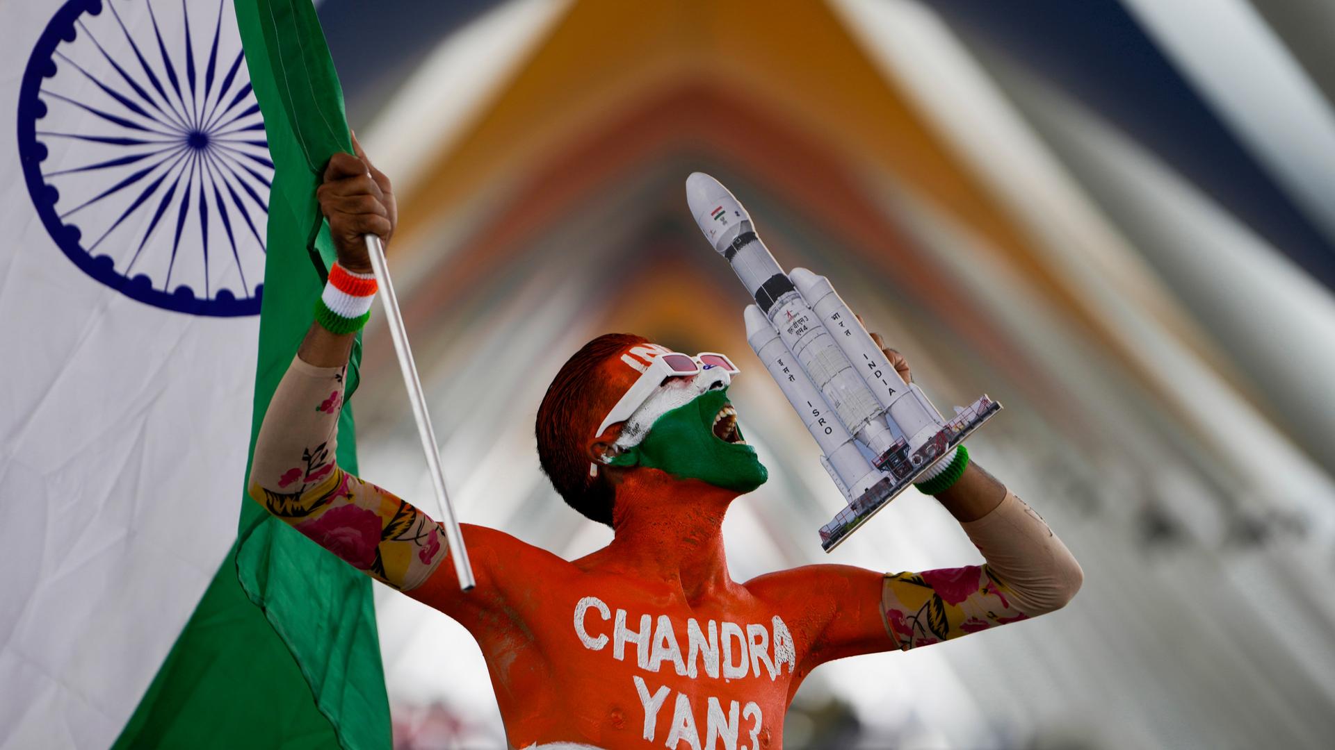 Ein mit der indischen Flagge sowie dem Schriftzug Chandrayaan-3 bemalter Mann hält eine indische Flagge und das Modell einer Weltraum-Rakete.