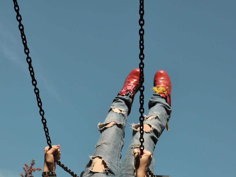 Eine Person mit Jeans schaukelt. 