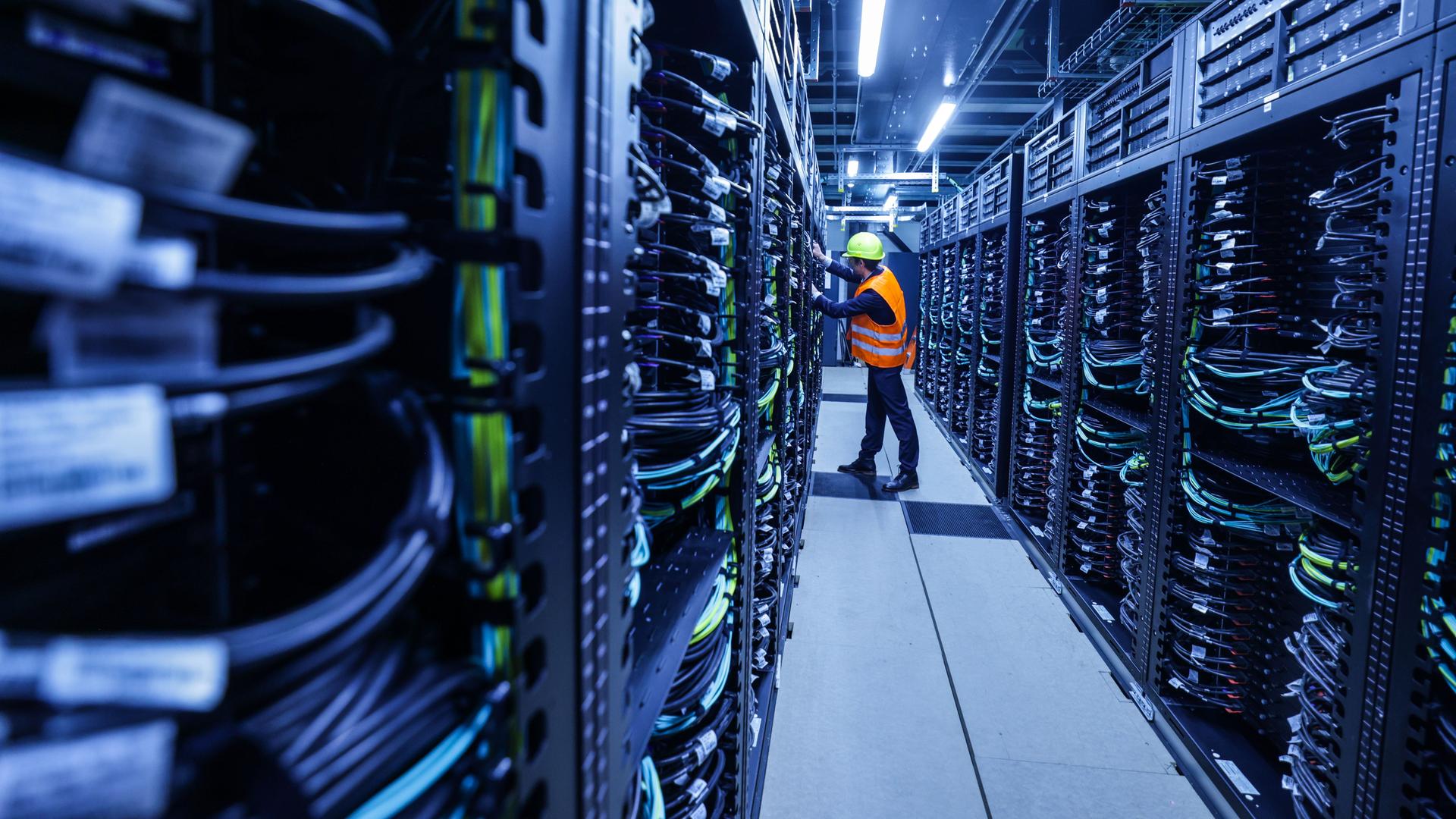 Ein Mitarbeiter arbeitet am Supercomputer Jupiter im Forschungszentrum Jülich. Er steht zwischen Unmengen an Datenkabeln. Ein Mitarbeiter arbeitet am Supercomputer Jupiter im Forschungszentrum Jülich. Er steht zwischen Unmengen an Datenkabeln.
