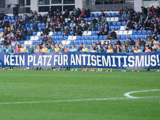 Spielerinnen von 1899 Hoffenheim und Werder Bremen mit einem Banner mit der Aufschrift "Nie wieder. Kein Platz für Antisemitismus" 
