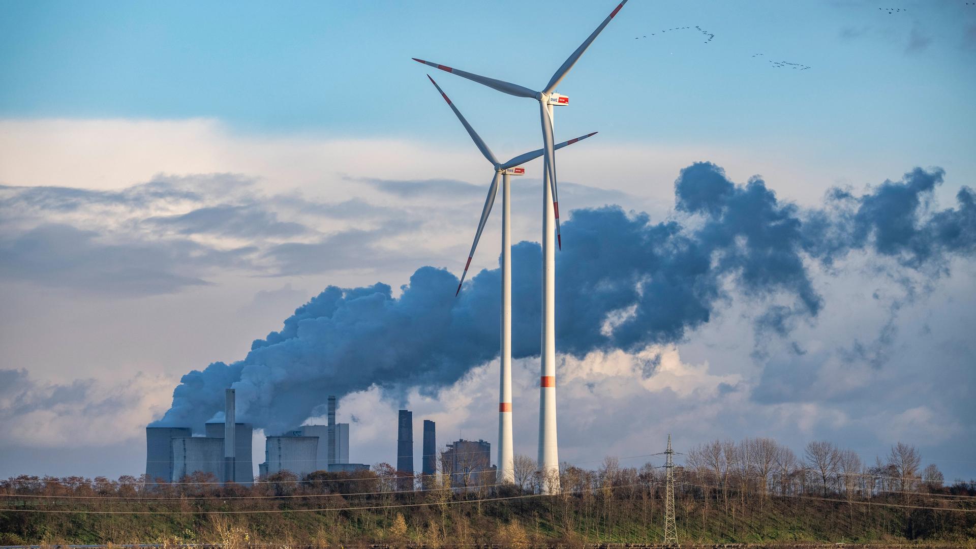 Foto des RWE Braunkohlekraftwerks Neurath, davor zwei Windräder