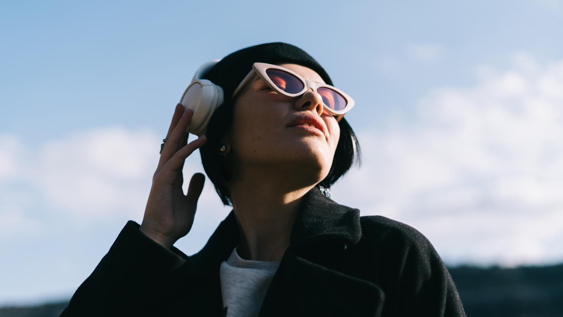 Eine junge Frau hört draußen in der Natur Musik über ihre Kopfhörer. Eine junge Frau hört draußen in der Natur Musik über ihre Kopfhörer.