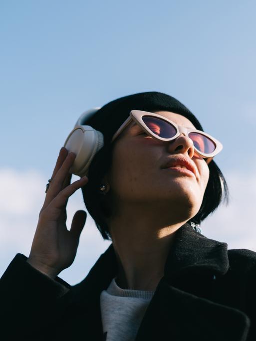 Eine junge Frau hört draußen in der Natur Musik über ihre Kopfhörer. 