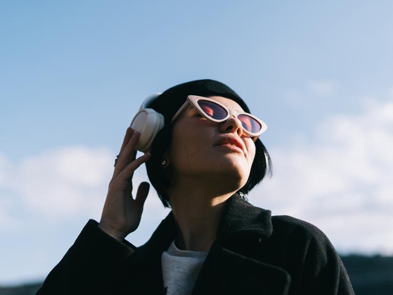 Eine junge Frau hört draußen in der Natur Musik über ihre Kopfhörer. 