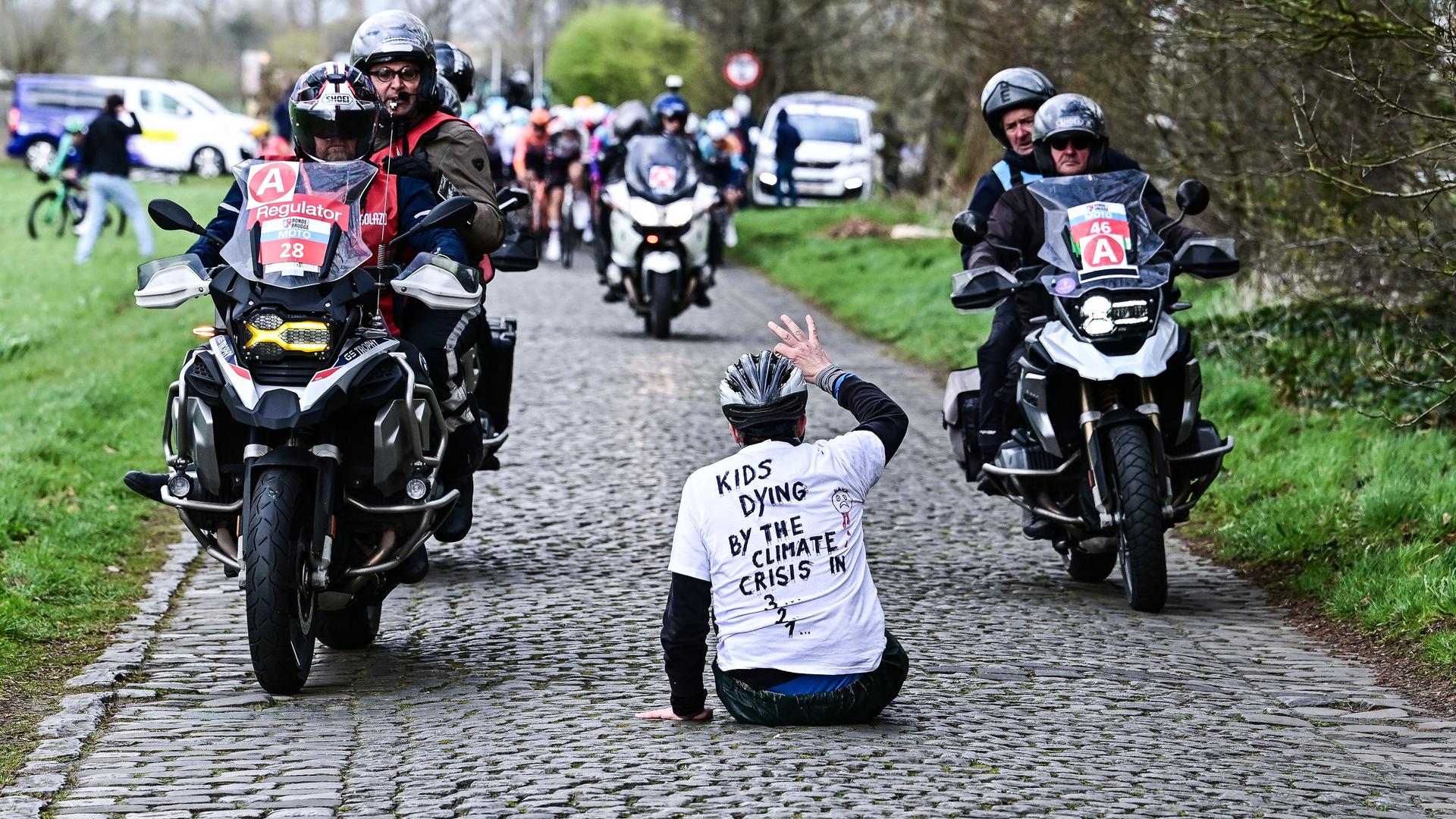 Brügge: Ein Klima-Demonstrant sitzt auf der Straße während des eintägigen Elite-Radrennens der Männer "Ronde van Brugge". Brügge: Ein Klima-Demonstrant sitzt auf der Straße während des eintägigen Elite-Radrennens der Männer "Ronde van Brugge".