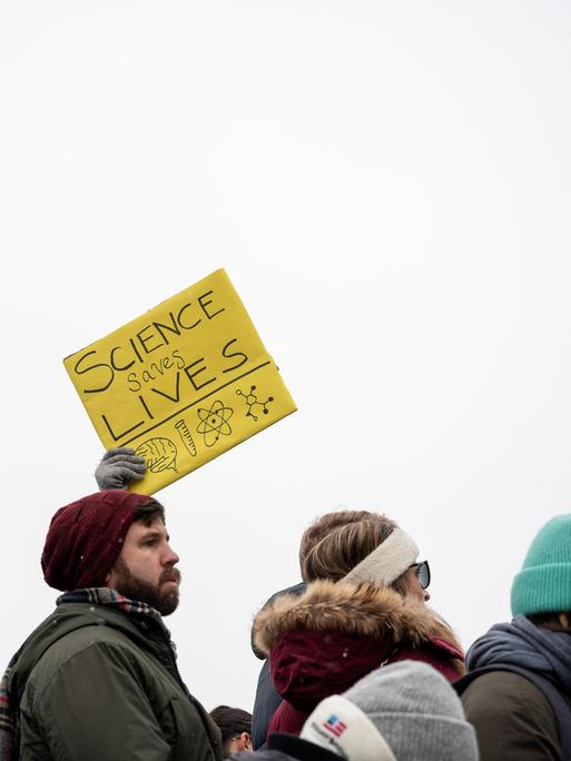 Protest von Wissenschaftlern, Forschern und ihren Unterstützern. Ein gelbes Schild wird in die Höhe gehalten. Darauf steht "Science saves lives", zu deutsch Wissenschaft rettet Leben.