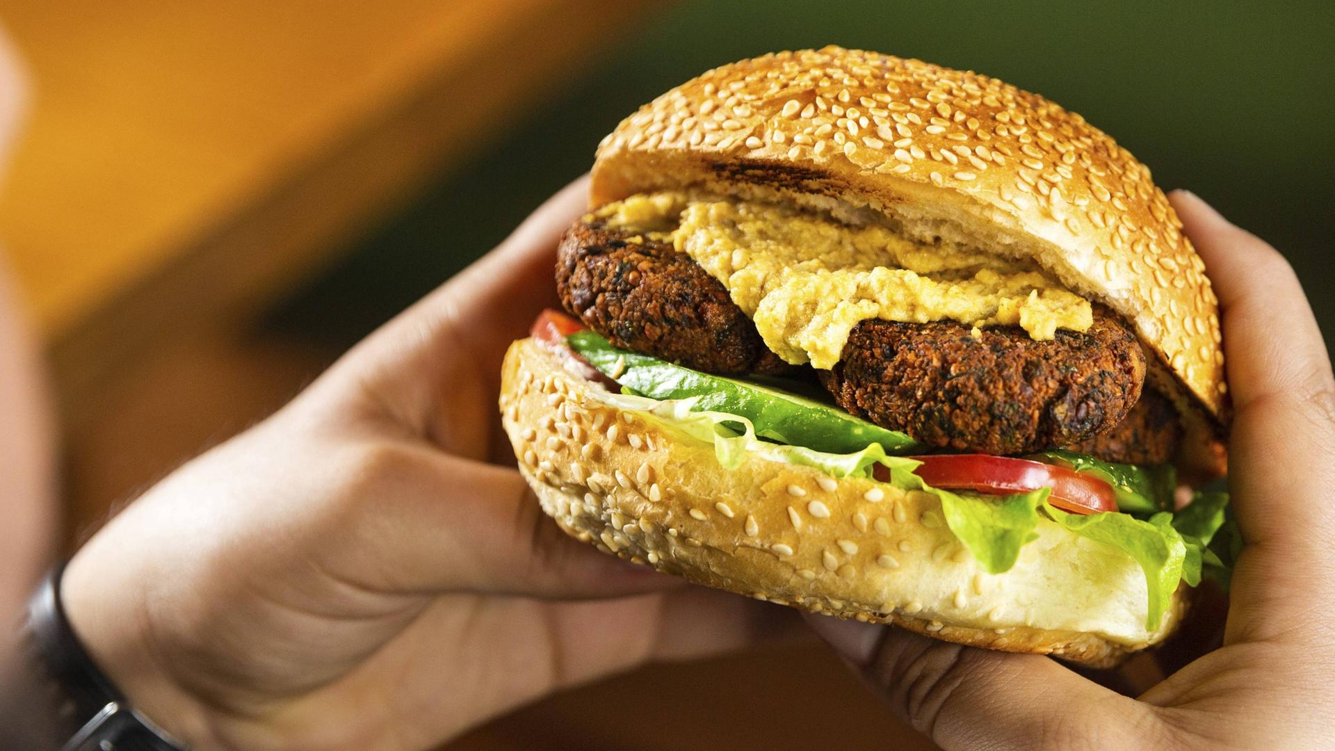 Zwei Hände halten einen Veggie Burger.