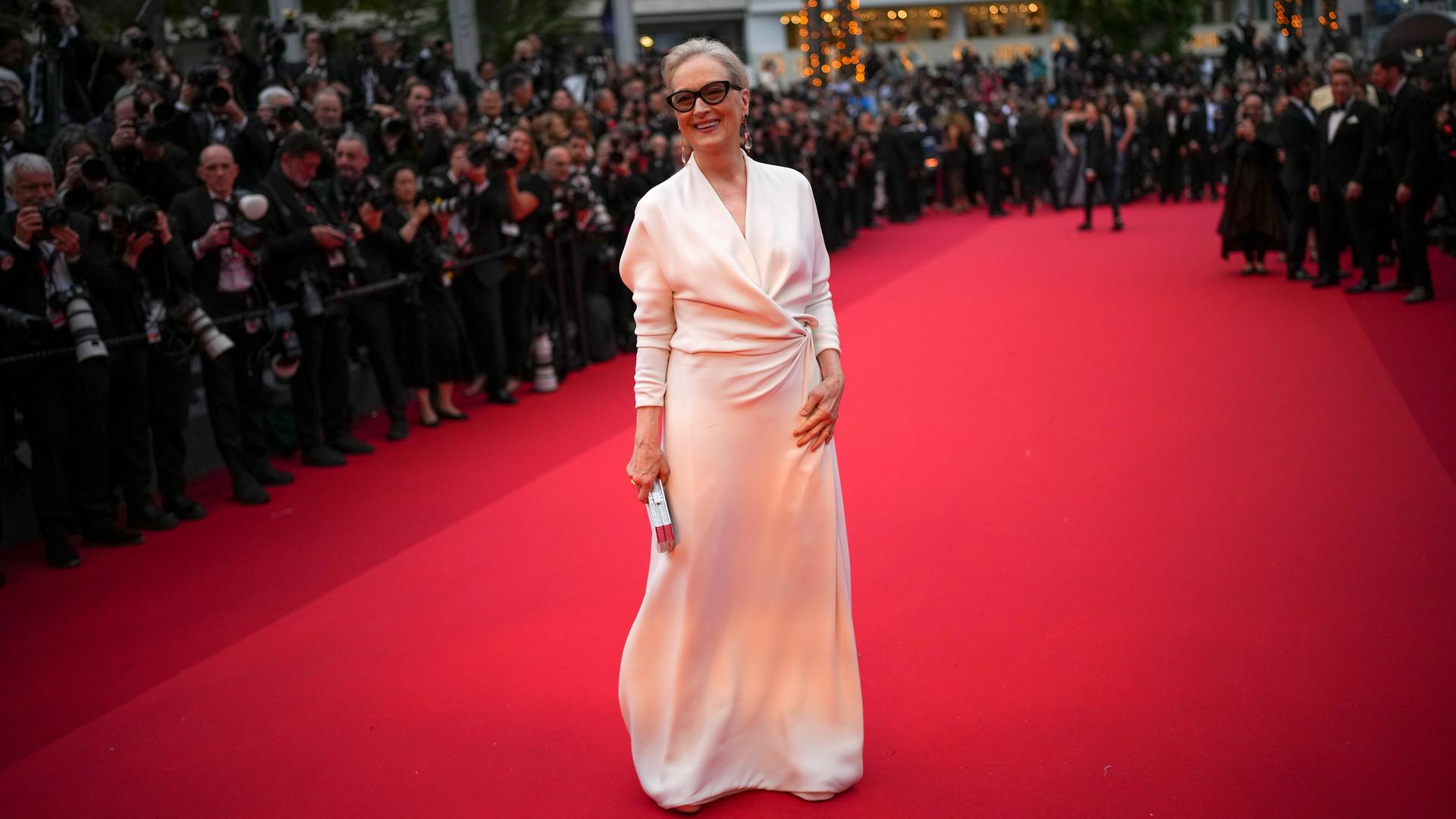 Das Foto zeigt Meryl Streep mit Sonnenbrille in einem weißen Kleid auf dem roten Teppich in Cannes.