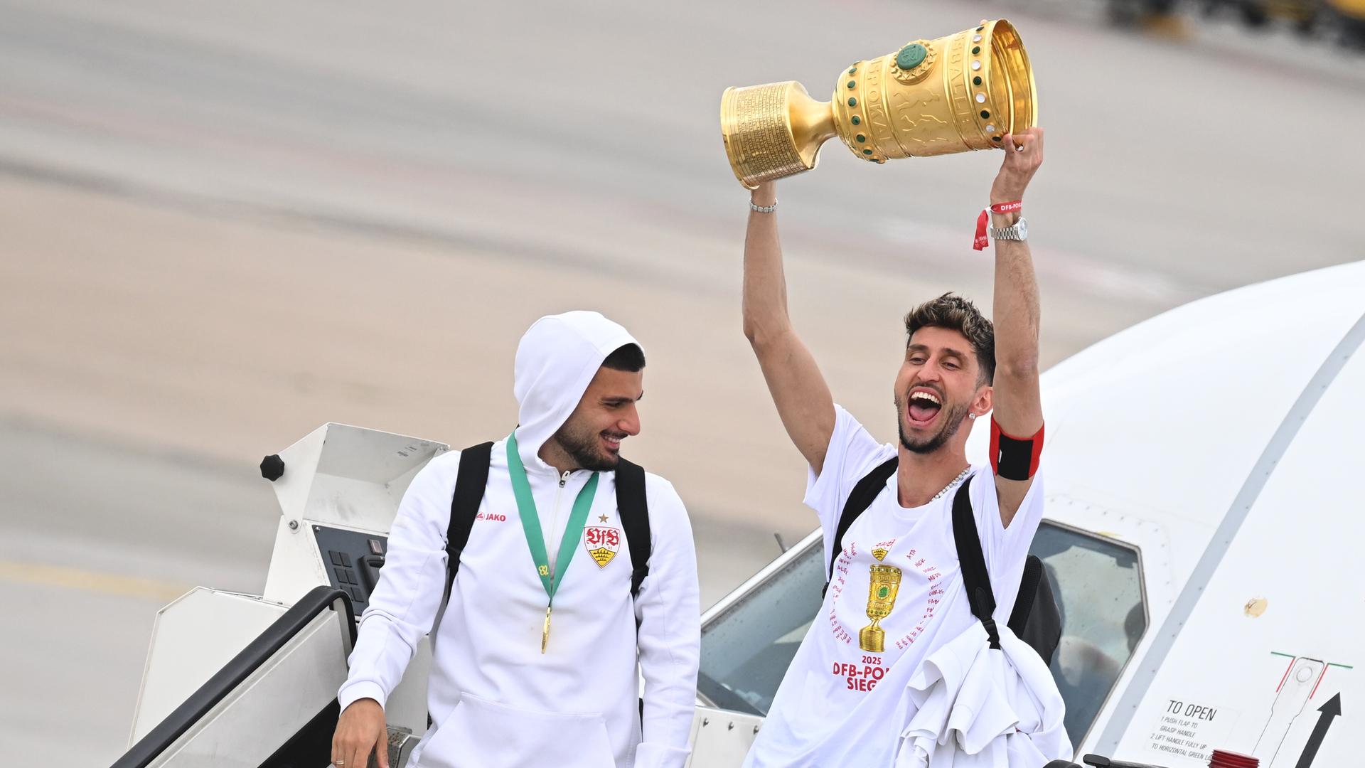 Fußball: DFB-Pokal, Arminia Bielefeld - VfB Stuttgart, nach dem Finale, Ankunft VfB Stuttgart am Flughafen. Atakan Karazor (r), Kapitän des VfB Stuttgart, jubelt nach der Landung mit dem DFB-Pokal neben dem Stuttgarter Deniz Undav.