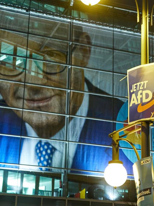 Ein Wahlplakat der AfD hängt vor der Parteizentrale der CDU, dem Konrad-Adenauer Haus. Im Hintergrund sieht man das Konterfei von Friedrich Merz auf dem Wahlplakat. 