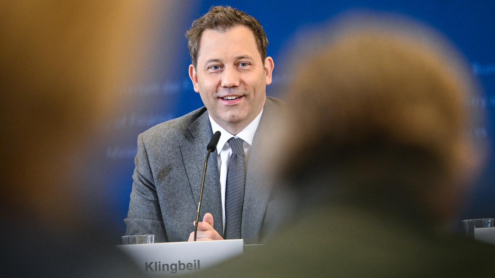 Lars Klingbeil spricht auf einer Pressekonferenz und sieht dabei sehr zufrieden aus. Vor ihm sind schemenhaft Umrisse von Menschen im Publikum zu sehen.