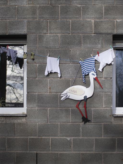 Ein Klapperstorch und Babykleidung an einem Wohnhaus zeigt die Geburt eines Kindes an. Bonn, 2021. 