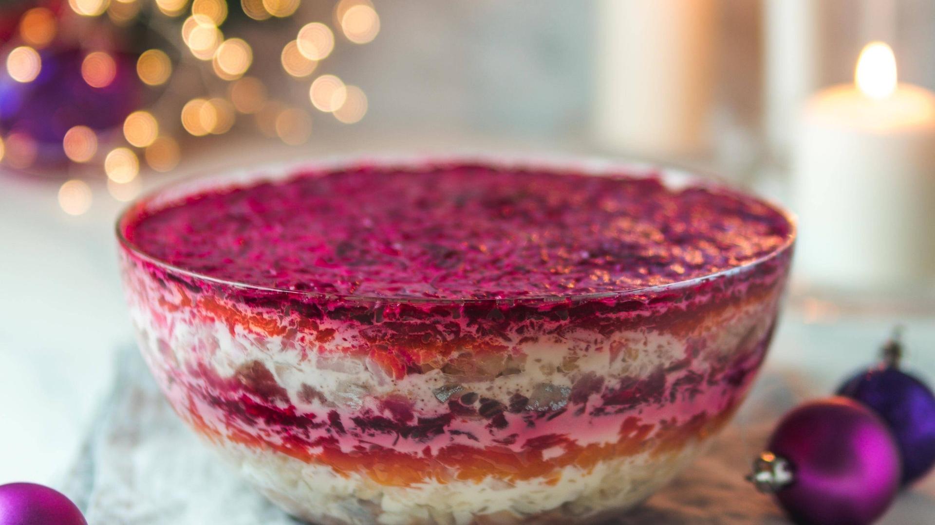 Ein festlicher Heringssalat, auch "Heringsmantel" oder "Pelzmantelsalat" genannt, steht vor ein paar Kerzen und Weihnachtdekoration